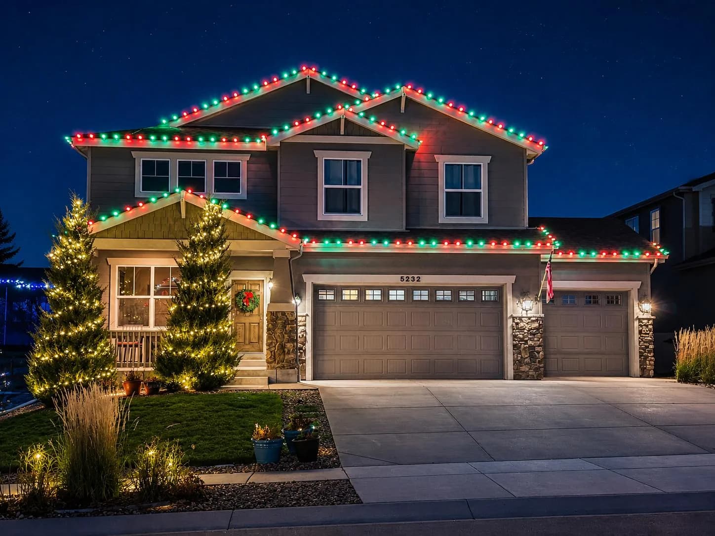 Red and green roofline lighting with lit evergreens on a two-storey Omaha-area home