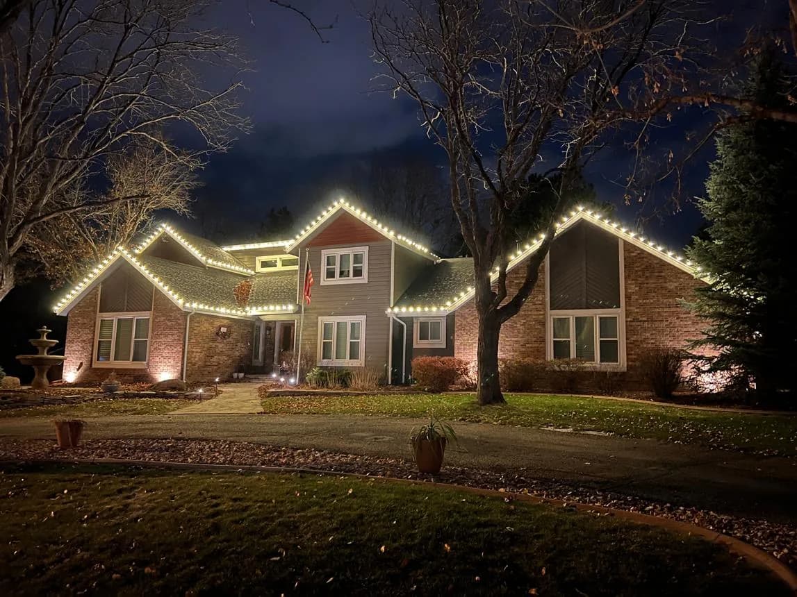 Warm white Christmas lights along the full roofline of a large Omaha-area home at dusk